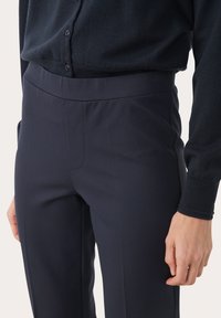 Pantalons ajustés bleu marine, en tissu lisse avec une taille élastique et des poches latérales. Coutures visibles près de la taille.