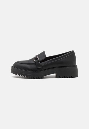 Sort læderloafer med kraftig rillet sål og metalspænde på vamp, vist i venstre sideprofil på hvid baggrund.