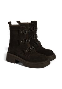 Braune Wildleder-Stiefeletten mit klobiger Sohle, ausgestattet mit mehreren dekorativen Riemen mit runden Beschlägen und Nieten an der Seite.