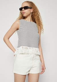 Fekete-fehér csíkos kötött felső frufrus szegéllyel, fehér, feltekert rövidnadrággal párosítva. A modellen elegáns dizájnú fekete napszemüveg van.