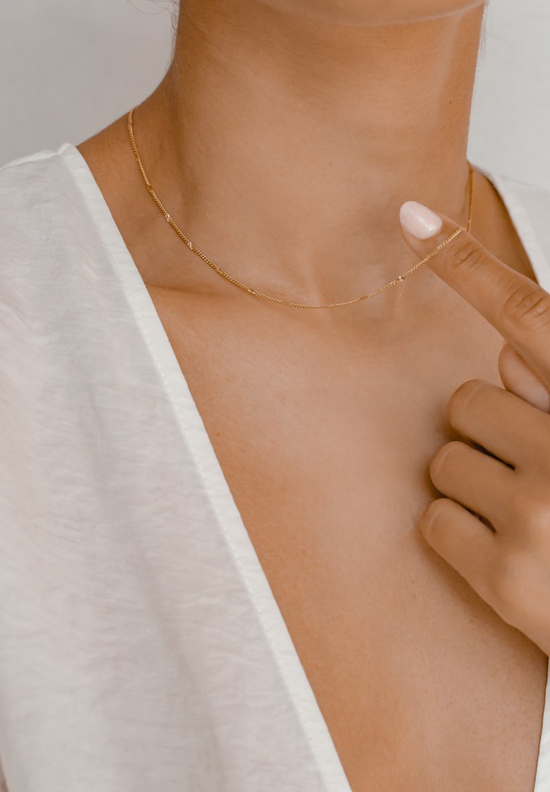 Collana in oro caratterizzata da un design delicato, anelli circolari e una superficie liscia, indossata sulla pelle nuda. Leggera, discreta e minimalista.