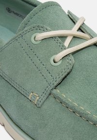 Scarpa verde in suede con design stringato, caratterizzata da una superficie testurizzata e cuciture beige a contrasto, e occhielli rotondi per i lacci.