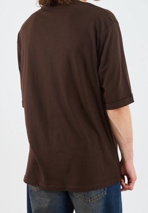 T-shirt en coton marron avec une coupe décontractée, manches courtes et revers roulés. Texture lisse, design simple, sans motifs ni graphiques.