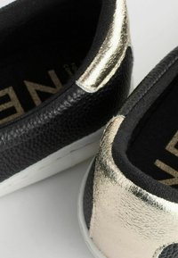 Svarta och guld sneakers med en strukturerad svart ovandel och metalliska guldaccenter på hälen, med en vit gummisula och mjuk futter.