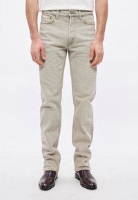 Gaiši pelēkas džinsu bikses ar klasisku taisnu kāju dizainu, ar smalku izbalējušu faktūru un standarta jostas cilpām. Zemāk brūnas ādas zābaki.