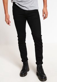 Jeans skinny negros de denim, con cremallera y cinco bolsillos. Se llevan con botas de combate negras con cordones.