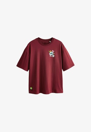 Dunkelrotes T-Shirt mit kurzen Ärmeln und Rundhalsausschnitt, das auf der Brust eine kleine bunte Grafik mit Totenkopf und Blumen zeigt und nahe dem Saum einen gelben "ok"-Aufnäher trägt.