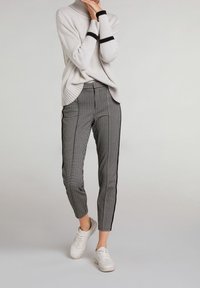 Maglione a coste grigio chiaro con dettagli a strisce nere abbinato a pantaloni tapered a quadri bianco e nero. Sneakers bianche completano l'outfit.