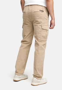 Beige kordflors cargobyxor med sidofickor, en avslappnad passform och textilstruktur. Bärs med vita sneakers.