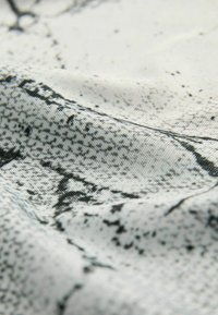 Gros plan d’un tissu texturé avec un motif abstrait gris et noir montrant de fins détails tissés et de légères rides.