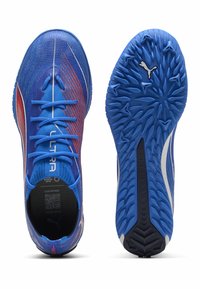 Niebieskie buty sportowe z siateczkową cholewką, z czerwonymi akcentami i teksturowaną gumową podeszwą. Widoczne sznurówki i elementy z logo na designie.