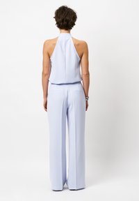 Lichtblauwe, mouwloze jumpsuit met een hoge hals en een losse, wijde pasvorm. Bevat achterzakken en heeft een gladde textuur.