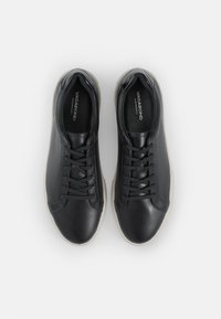 Sneaker neri in pelle, con design a lacci, texture liscia e suola in gomma bianca. Branding visibile all'interno della scarpa.