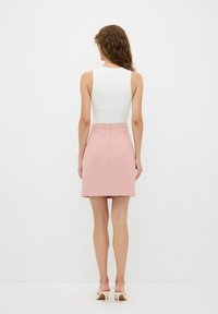 Top blanco sin mangas combinado con una mini falda rosa claro. La falda tiene una textura suave y un diseño simple. Cierre de cremallera en la parte posterior.