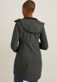 Grijze, lange mouwen jas gemaakt van zacht, gestructureerd materiaal met een capuchon. Heeft een getailleerde taille en subtiele stikseldetails voor extra vorm.