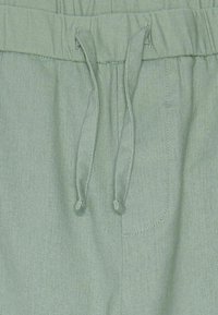 Helles grünes, weiches Stoffbund. Kordelzug-Verschluss mit Schlaufenenden, kleine Seitentasche mit Steppnähten, lässiger Schnitt.