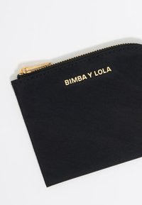 Melnas neilona soma ar zelta toņa rāvējslēdzēju. Priekšpusē ir iegravēts "BIMBA Y LOLA" logo. Vienkārša taisnstūra forma. Gluda tekstūra.