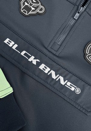 Donkergrijs sporttop met een rits, met witte geborduurde branding "BLCK BNNS" en zwarte en groene accenten met dierenvormige patches.