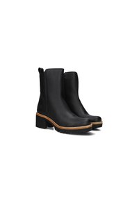 Botas negras de cuero hasta el tobillo con una suela de goma gruesa, que presentan un acento marrón claro en la base y un pequeño lazo en la parte superior para facilitar su uso.