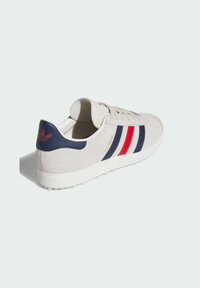 Sneakers with a beige suede upper, navy heel, and three stripes in red and navy. Features a white rubber sole with textured detailing.