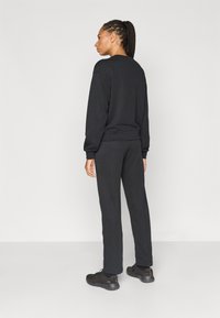 Σετ μαύρη φούτερ μπλούζα και παντελόνι φόρμας, με άνετη εφαρμογή. Το ύφασμα είναι απαλό με ριμπ μανσέτες και μέση. Μαύρα παπούτσια ολοκληρώνουν την εμφάνιση.