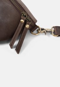 Hnědá kožená taška s dvěma bronzovými zipy, s texturovaným povrchem a kovovým klipem pro připevnění. Viditelný nastavitelný kožený popruh.