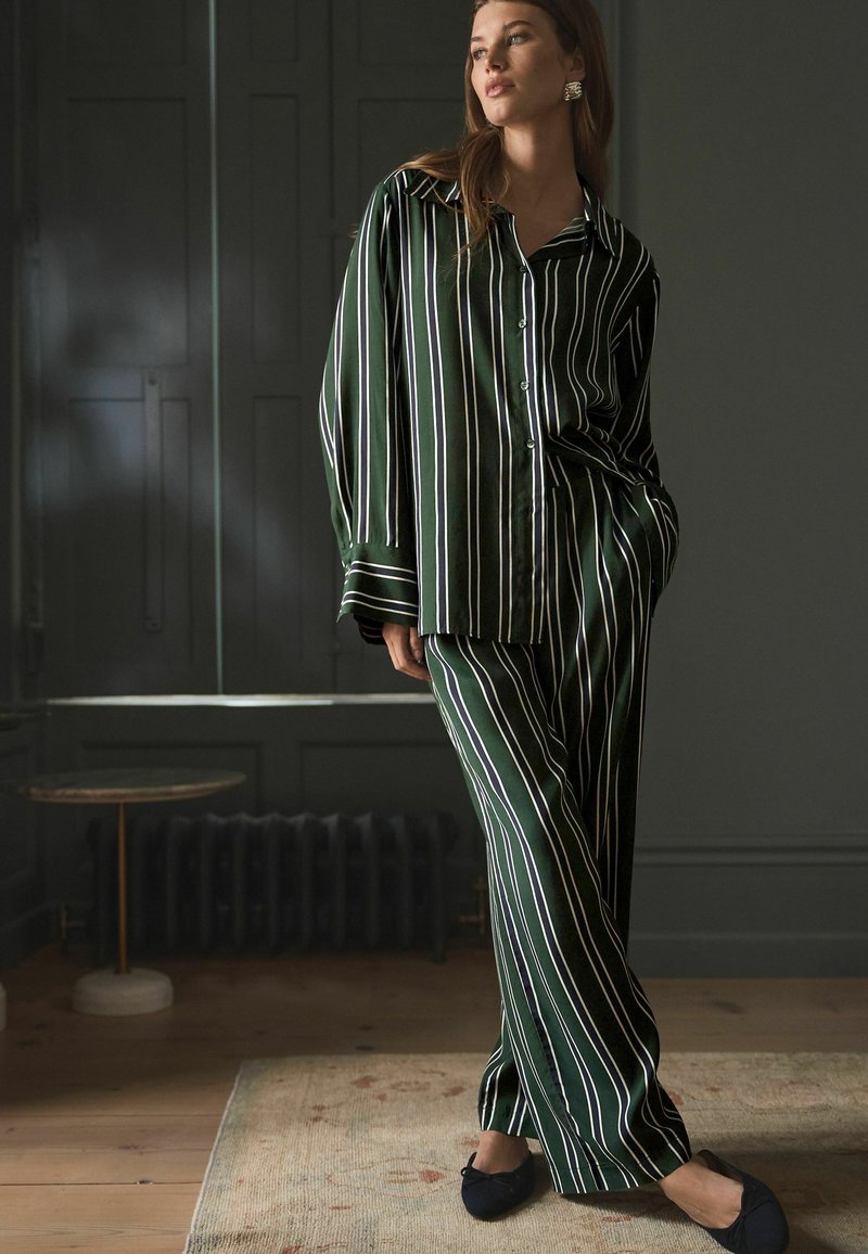 Grøn- og hvidstribet satin pyjamas sæt med knap-åben skjorte og brede bukser. Blød tekstur med løs pasform og dybe manchetter.
