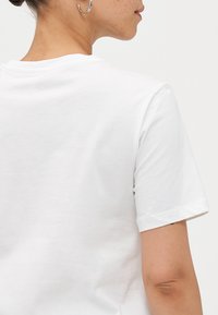 White cotton t-shirt showing a relaxed fit with a crew neckline. Short sleeves and visible stitching detail on the hem.