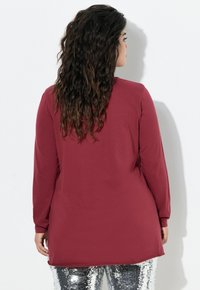 Bordeaux lange mouw tuniek met een vloeiende uitstraling, gecombineerd met glanzende zilveren paillettenbroeken, met een ronde hals en een gebogen zoom.