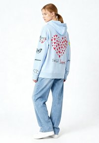 Sweat à capuche bleu clair avec graphiques de cœur rouge, papillons et texte en écriture cursive. Associé à un jean en denim léger et ample, et des baskets blanches.