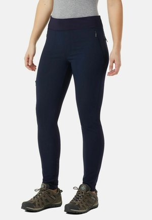 Dunkelblaue Leggings mit einem breiten Bund, schlankem Design, seitlichen Taschen und glatter Textur, kombiniert mit braunen Wanderschuhen.