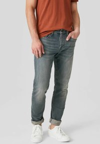 Ljusblå tampade jeans med en urblekt finish, med midjehöjd, fem fickor och uppvikta fållar, parat med vita sneakers.