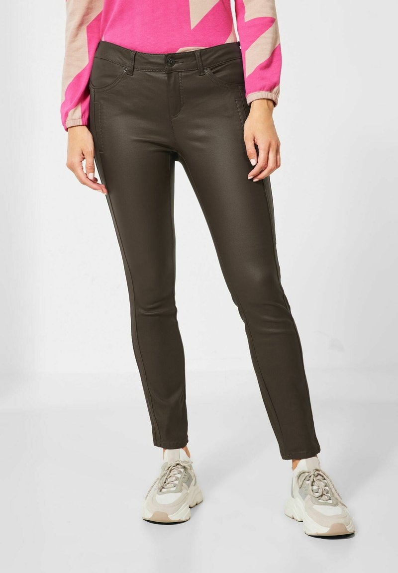 Pantalons en simili cuir marron foncé avec une coupe ajustée, dotés de poches avant et de détails de surpiqûres discrètes sur les côtés, associés à des baskets claires.