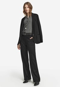 Svart skräddarsydd kavaj över en grå topp, i kombination med lösa svarta byxor och svarta högklackade skor. Inkluderar ett långt silverhalsband.