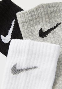 Tre par Nike-strumpor i svart, grått och vitt. Varje par har en kontrasterande logotyp. Strumporna har en ribbad textur och en klassisk design.