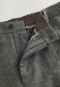 Gray textured trousers with a check pattern, featuring a brown elastic waistband and button closure, alongside a zipper and pocket details.