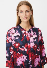 Florale Bluse mit rotem, pinkem und navy Muster, langen Ärmeln, rundem Ausschnitt, strukturiertem Stoff und Knopfverschluss.