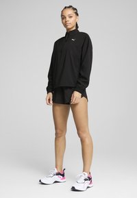 Sort, lynlåset sportjakke med lange ærmer, parret med sorte shorts. Hvide og lyserøde sneakers med sorte detaljer fuldender outfittet.