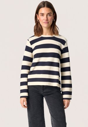 Marineblå og cremefarvet stribet sweater med lange ærmer, rund halsudskæring og struktureret ribbet stof. Sammen med mørkegrå bukser.