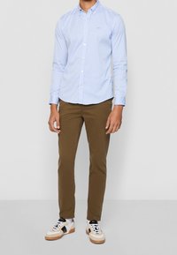 Ljusblå och vit randig skjorta med knappar, bruna slim-fit byxor och vita sneakers med svarta och beige detaljer. Inga synliga mönster.