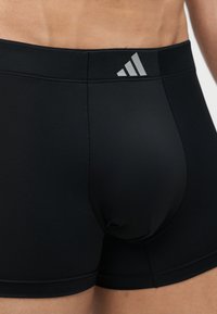 Κοντινό πλάνο ενός ατόμου που φοράει μαύρα αθλητικά μποξεράκια με μικρό, ανακλαστικό λογότυπο Adidas στη ζώνη μέσης.