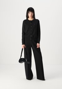 Zwarte cardigan met knopen en lange mouwen, gecombineerd met hoge zwarte broeken en een glanzende zwarte handtas. Eenvoudig ontwerp en texturen.