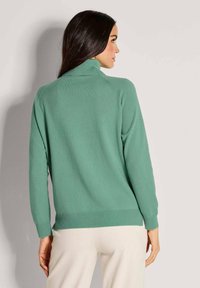 Grüner Strickpullover mit hohem Kragen, langen Ärmeln und Rippbündchen. Weiche Textur und lockere Passform. Schlichtes Design, ideal zum Lagenlook.