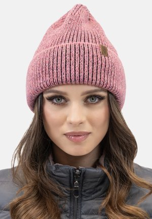 Gorro de punto rosa con una parte superior puntiaguda y textura acanalada, con una pequeña etiqueta de cuero marrón. Se lleva con una chaqueta gris con cremallera.