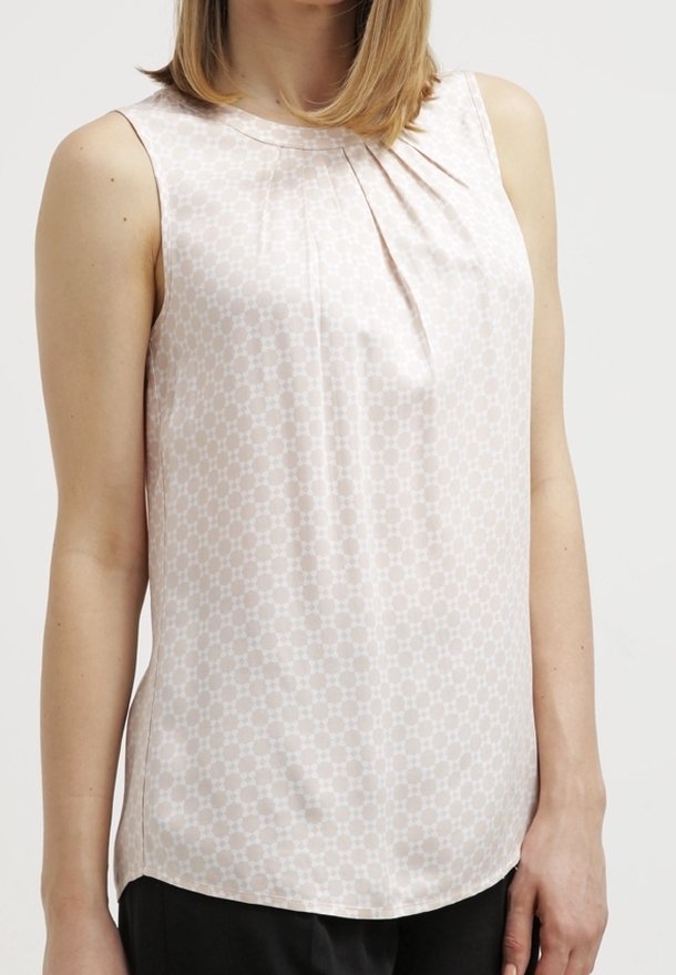 Hihaton vaaleanpunainen pusero, jossa on hienovarainen geometrinen kuvio, pyöreä kaula-aukko ja pieniä frilloja edessä, yhdistettynä mustiin housuihin.