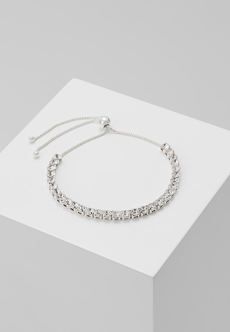Bracelet en argent ajustable avec une seule rangée de cristaux ronds transparents et une fermeture coulissante sur un bloc d'affichage blanc.