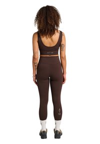Brun atletisk sæt bestående af en tætsiddende crop top og højtaljede leggings. Toppen har en lav scoop ryg, og begge dele viser "ATW" logoet.