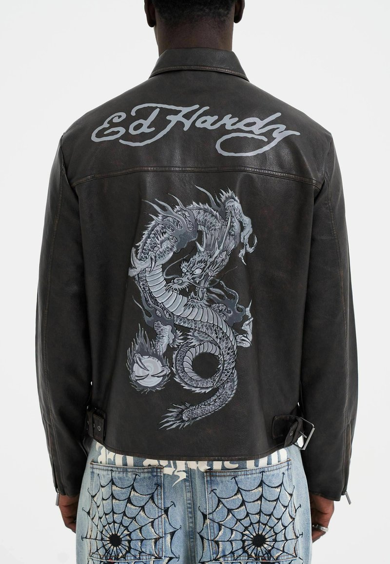 Svart läderjacka med en stor grå drakgrafik på baksidan och "Ed Hardy"-text; har en krage och justerbara midjestrimlor.