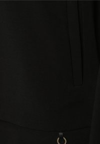 Hoodie noir avec une texture lisse et mate, comportant une poche latérale et un accent décoratif en métal doré au niveau de l'ourlet.