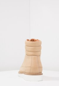 Beżowe zamszowe botki za kostkę z opadającym kołnierzem, wyściełanym wnętrzem i białą gumową podeszwą. Posiadają haftowane detale wzdłuż boków.